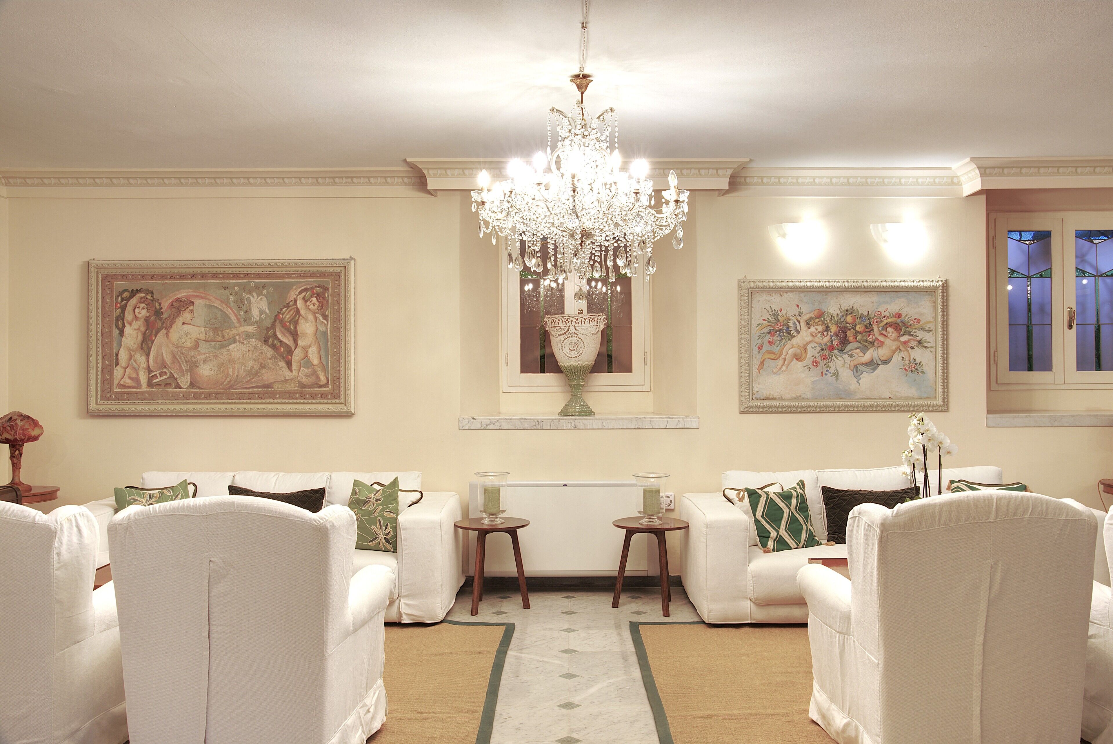 A spacious living room with white furniture, a chandelier, and two paintings on the walls.