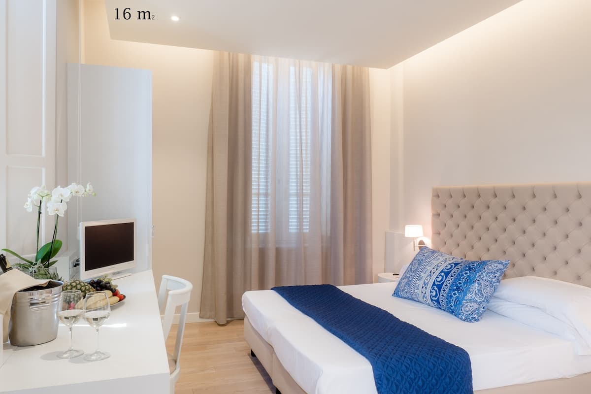 A modern hotel room with a large bed, a desk with a computer, and a window with sheer curtains.