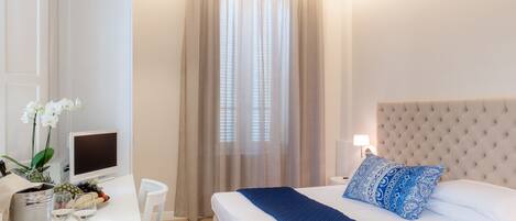 Una habitación de hotel moderna con una cama grande, un escritorio con computadora y una ventana con cortinas ligeras.