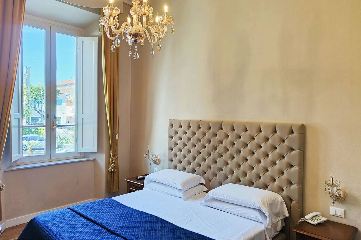 A bedroom with a large bed, a chandelier, and a view of the outside.
