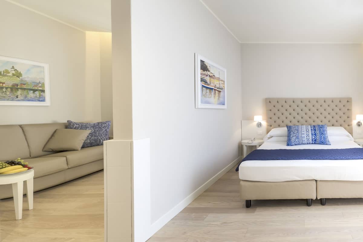A modern bedroom with a large bed, a sofa, and a small table with fruit.