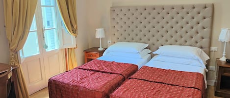 Una habitación de hotel con una cama grande, dos mesitas de noche, una ventana con cortinas y suelo de madera.