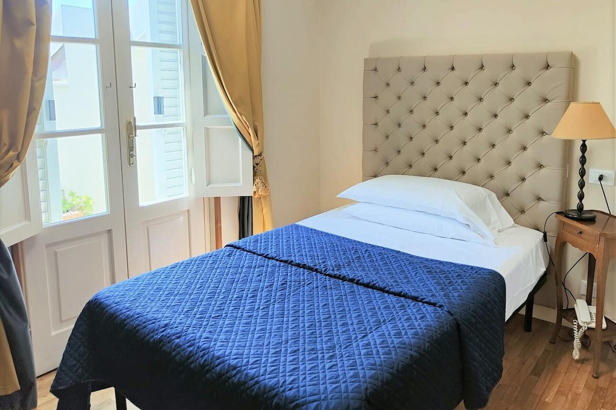 A bedroom with a bed, a nightstand, a lamp, and a window with curtains.