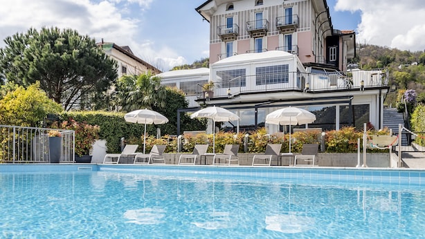 A poolside area with lounge chairs and umbrellas, a large building with balconies, and a clear sky.