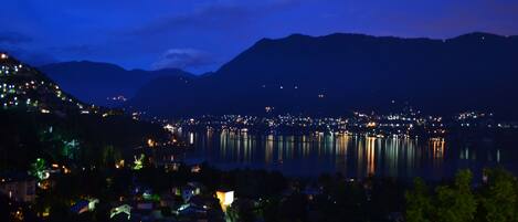 A nighttime view of a city with a lake, mountains in the background, and illuminated buildings.