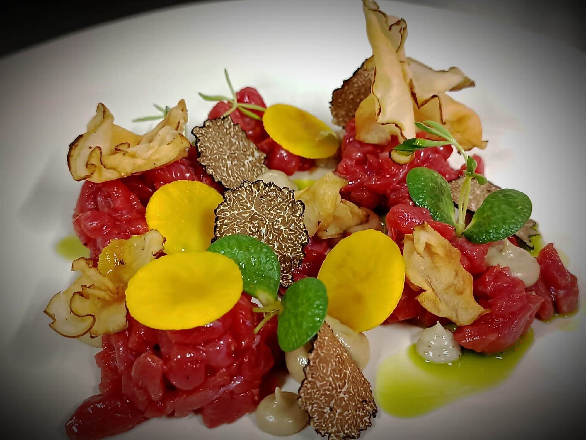 A dish with various ingredients including red meat, mushrooms, and yellow elements, possibly cheese or fruit, on a white plate.