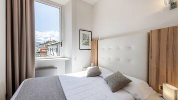 Quarto de hotel com uma cama grande, janela com cortinas, mesa de cabeceira com abajur e um quadro na parede.