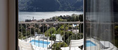 Un balcón con sillas blancas que da a un lago, montañas y un pueblo.