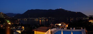 Vista nocturna de un pueblo costero con zona de piscina, montañas al fondo y edificios iluminados.
