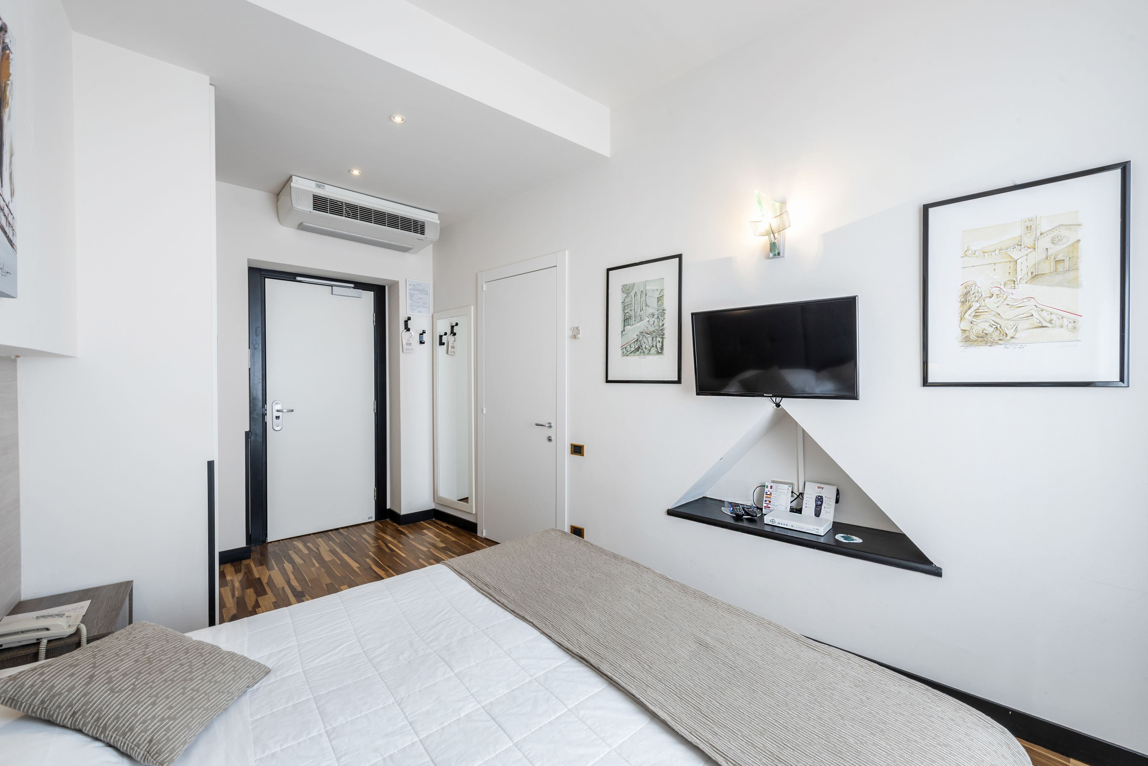 Ein modernes Hotelzimmer mit einem Bett, einem an der Wand befestigten Fernseher und Kunstwerken an den Wänden.