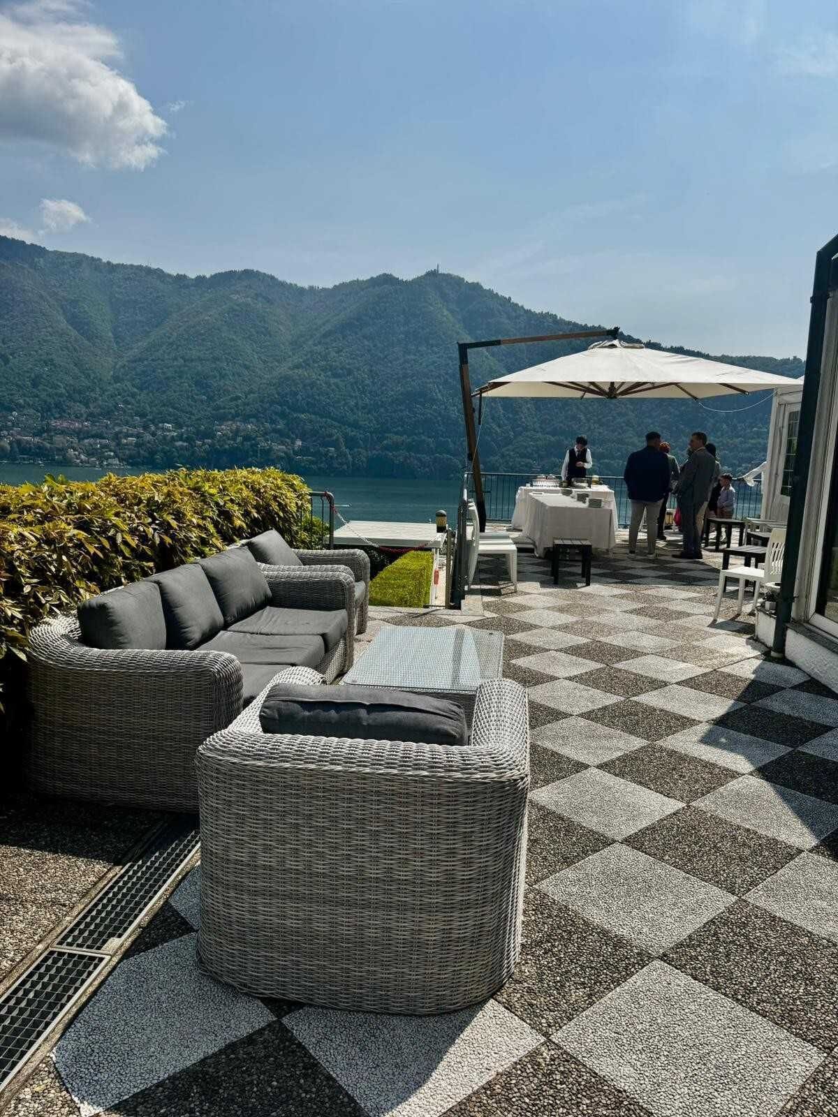 Een terras met rieten meubels, een geruit vloertje en uitzicht op bergen en een meer.
