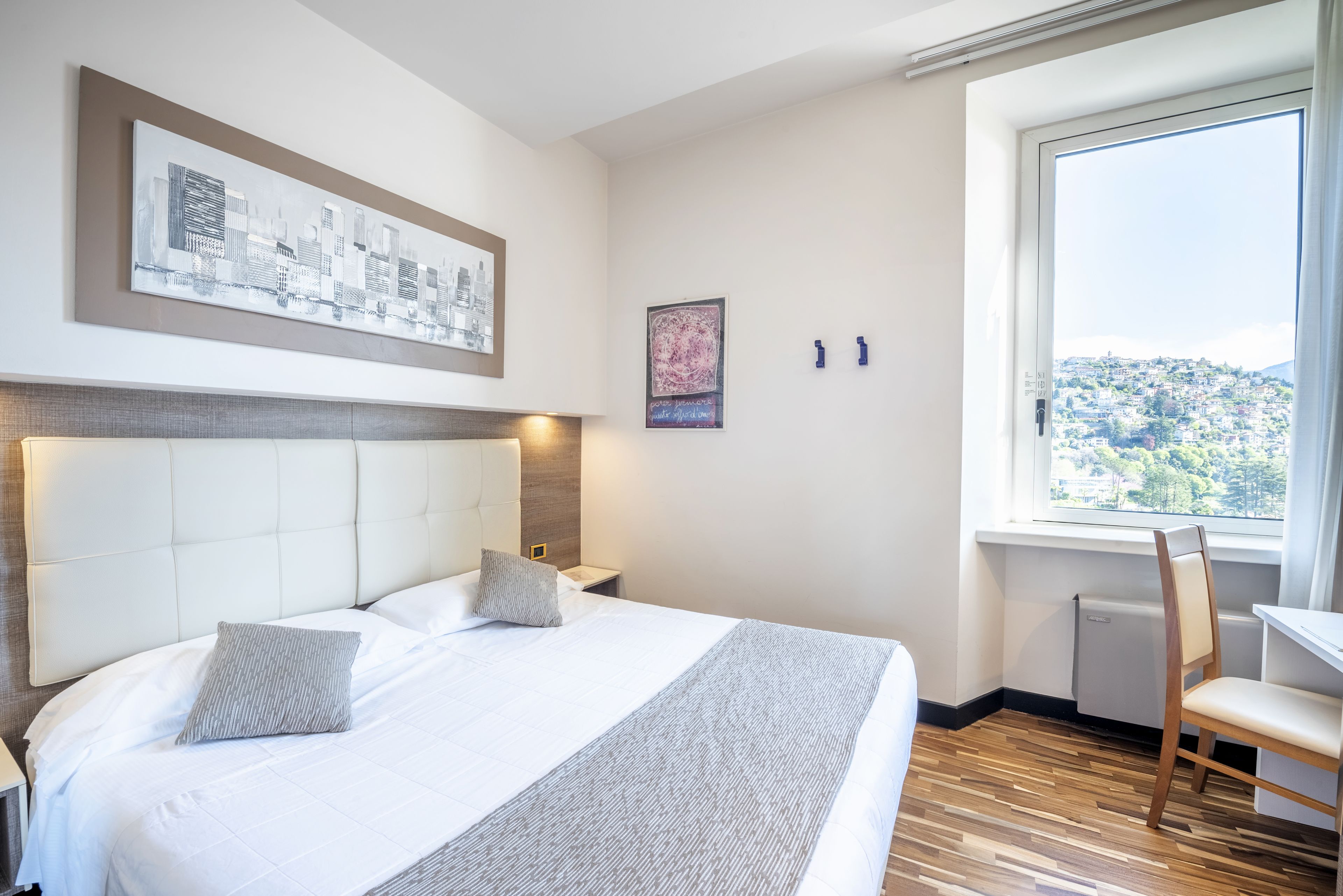 Hotelkamer met een groot bed, uitzicht op een stadsgezicht en een raam met uitzicht op een heuvel.