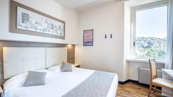 Habitación de hotel con una cama grande, vistas a un paisaje urbano y una ventana con vista a una colina.