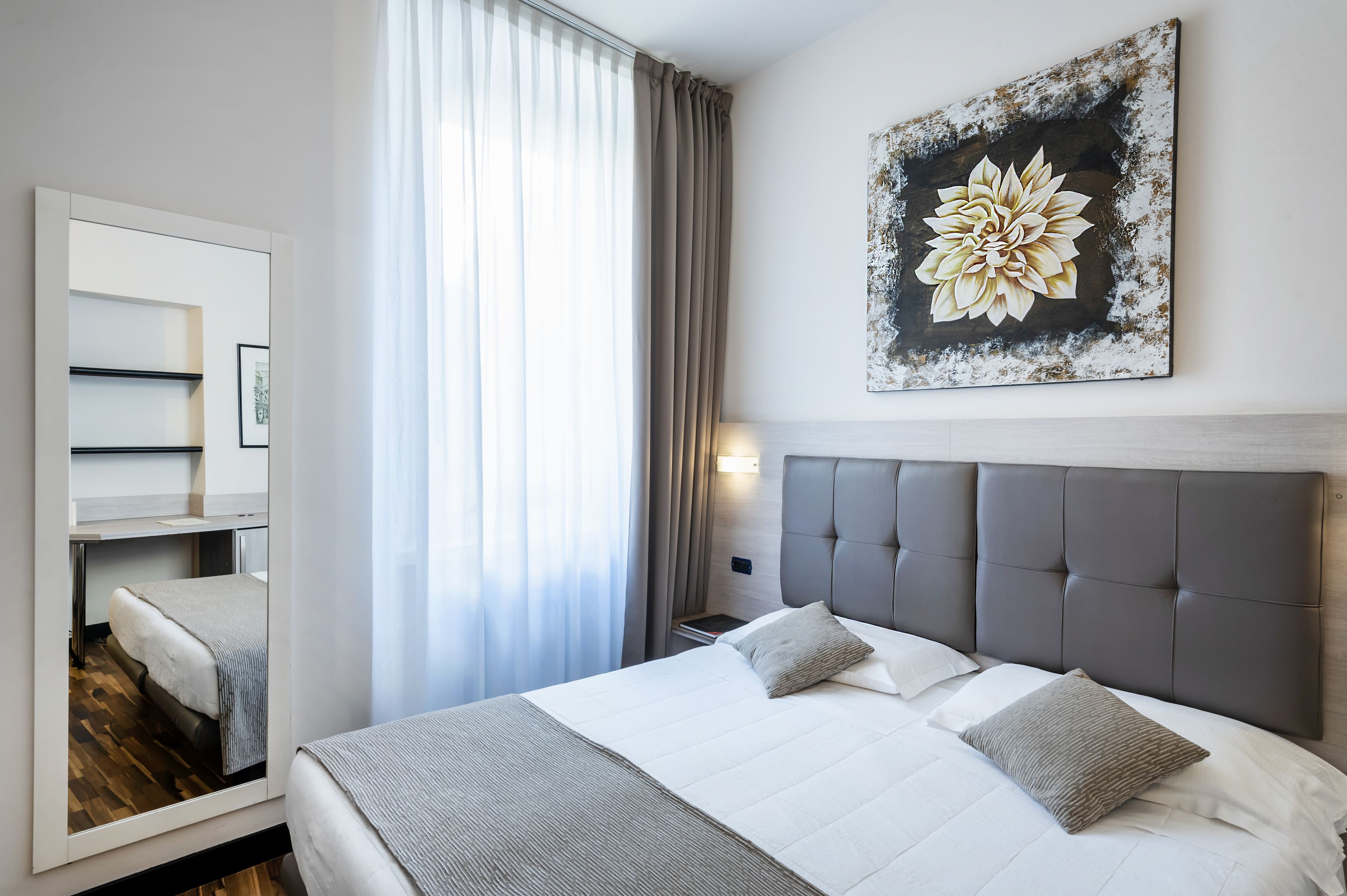 Una camera d'albergo moderna con un letto grande, uno specchio, un comodino e un'opera d'arte appesa al muro.