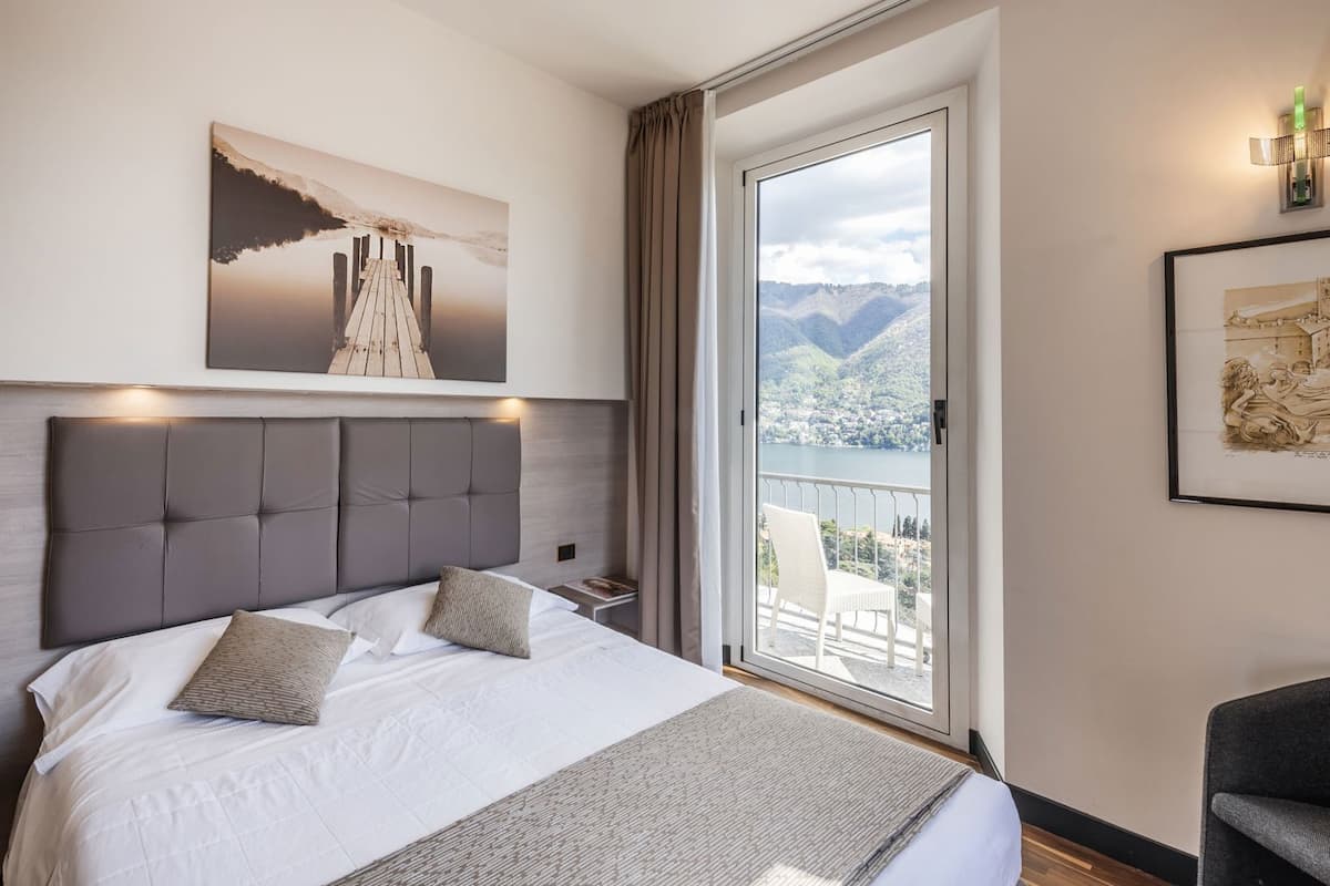 A hotel room with a large bed, a view of mountains through a balcony, and artwork on the walls.