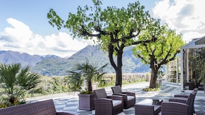 A terrace with wicker furniture and a checkered floor, overlooking a mountainous landscape.