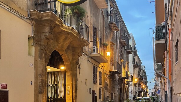 A narrow street with a hotel sign, stone archway, and potted plants lining the sidewalk.