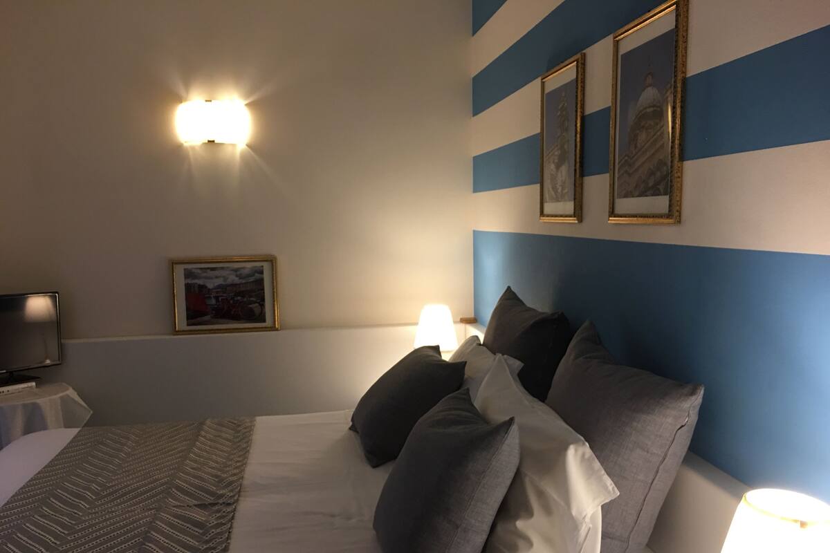 A hotel room with a bed, a TV, and a wall with framed pictures.