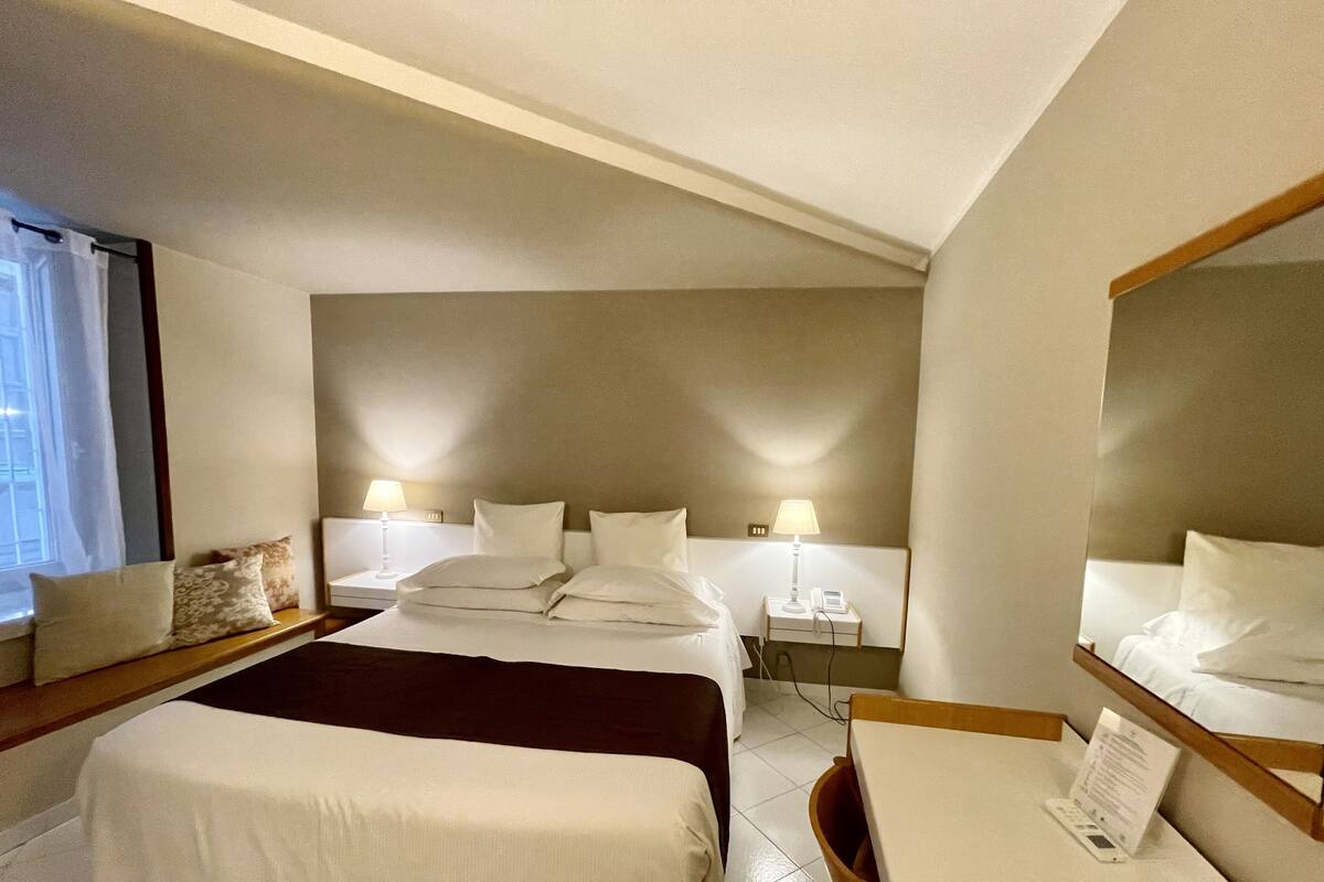A hotel room with a large bed, bedside tables, a desk, and a mirror.