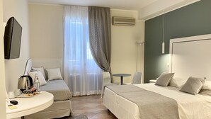 A hotel room with two beds, a desk with a kettle, a chair, a small table, and a TV.