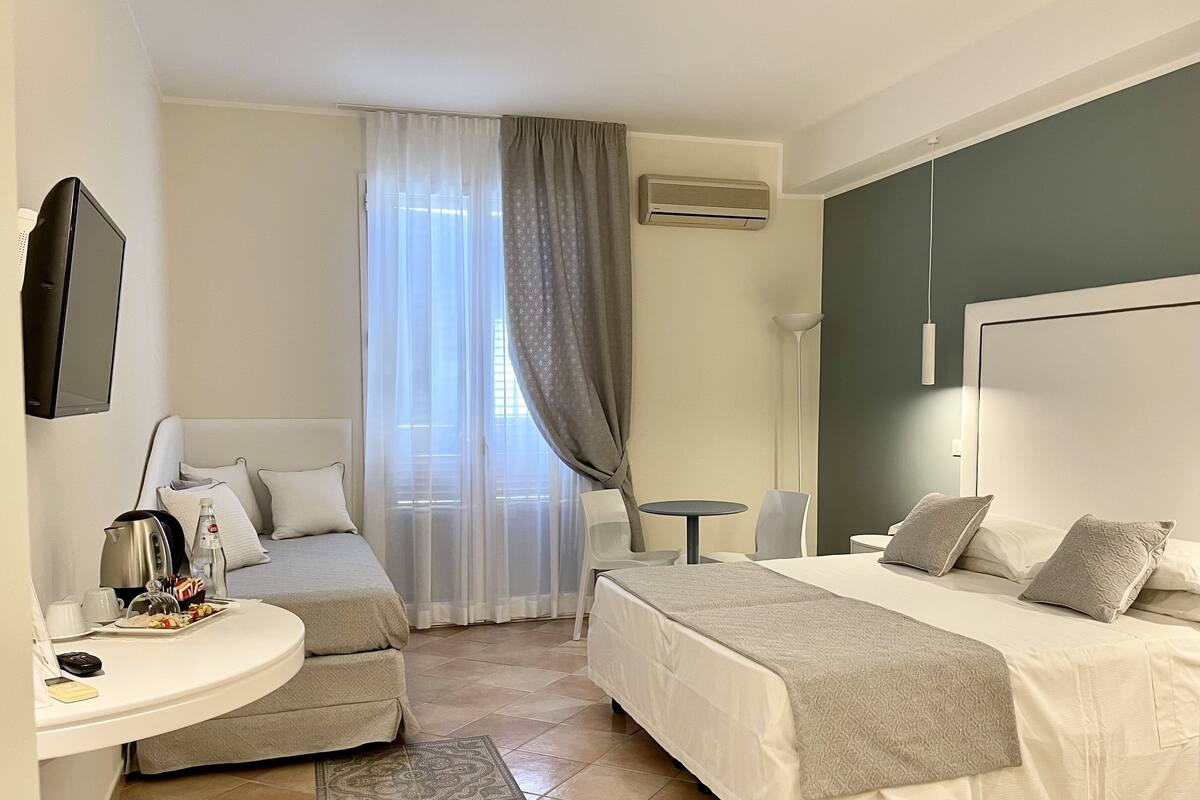 A hotel room with two beds, a desk with a kettle, a chair, a small table, and a TV.