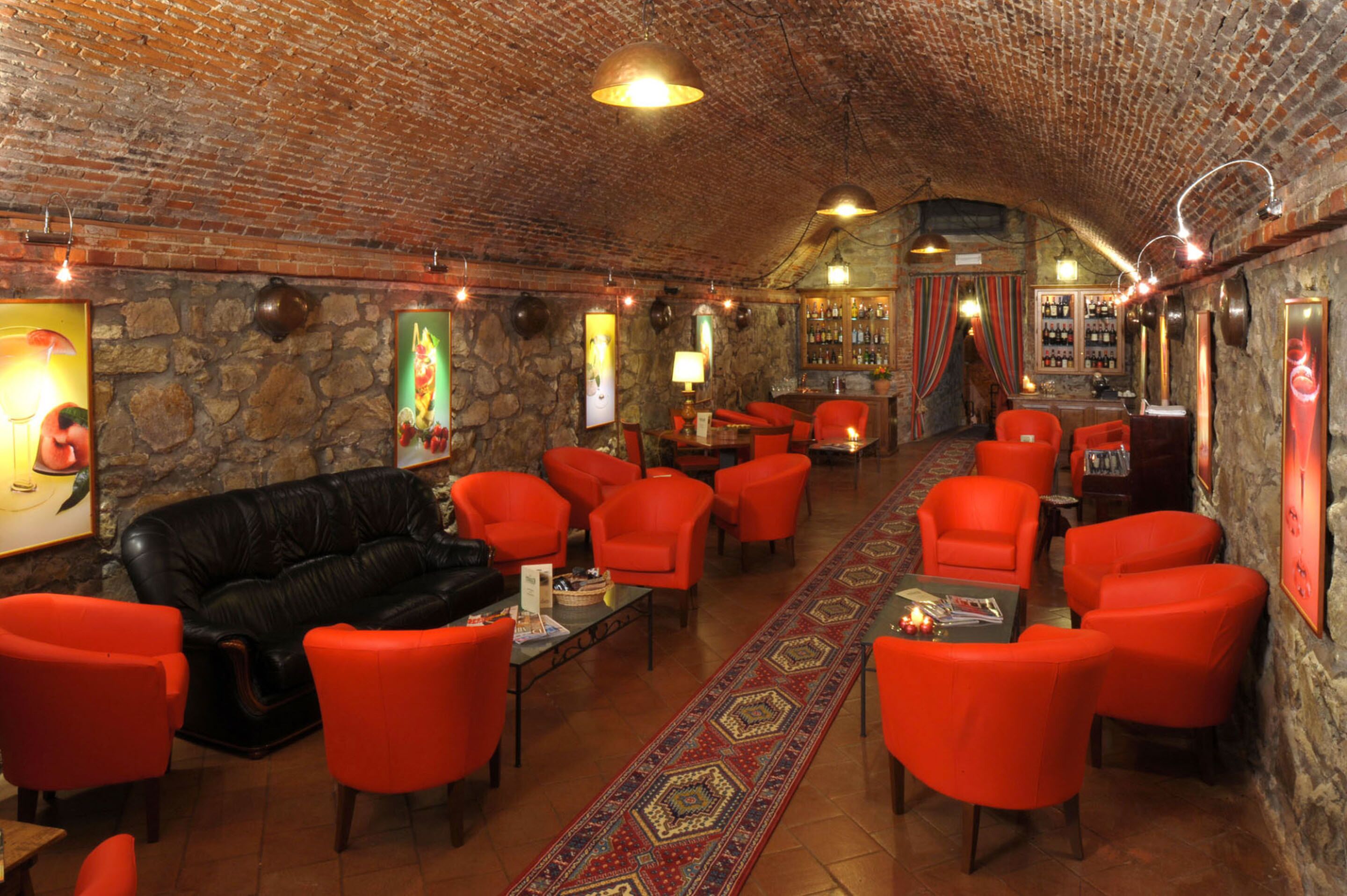 A cozy lounge with brick walls, a stone fireplace, and red upholstered chairs.