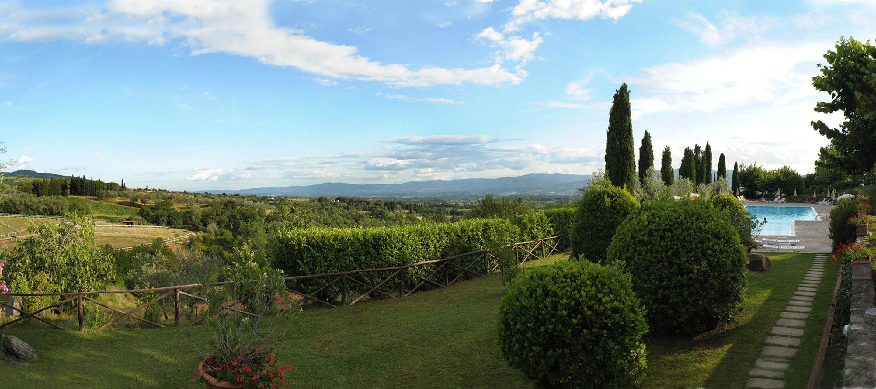 A garden with a pool, a view of the countryside, and a clear sky.