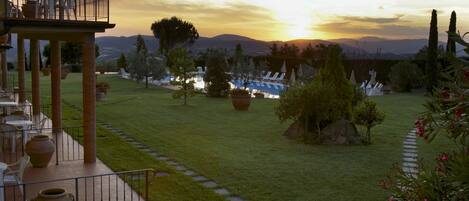 Eine Terrasse mit Sitzgelegenheiten und Blick auf den Sonnenuntergang über einem angelegten Garten.