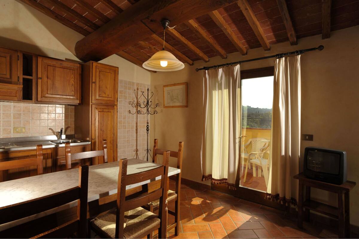 Eine Küche mit Holzausstattung, einem Esstisch mit Stühlen, einer Kristallleuchter und einem Blick ins Freie durch ein Fenster mit Vorhängen.