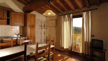 Una cocina con armarios de madera, una mesa de comedor con sillas, una araña y vistas al exterior a través de una ventana con cortinas.
