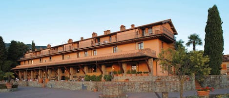 A large, multi-story building with a terracotta facade, multiple balconies, and a courtyard with stone walls and potted plants.