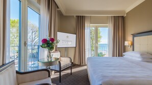 A hotel room with a bed, a chair, a small table with a vase of flowers, a TV, and a balcony with curtains.
