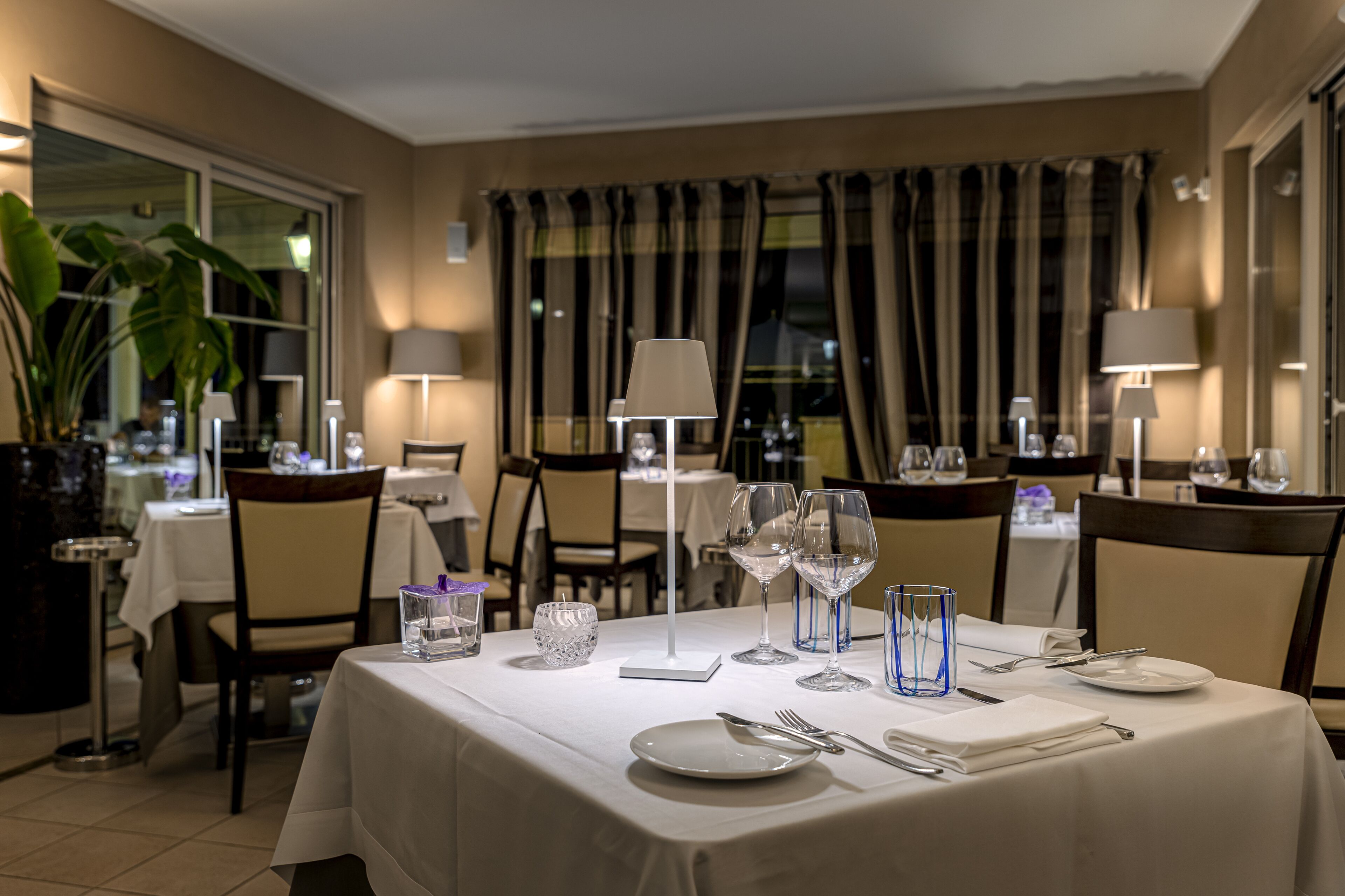 A dining area with a table set for two, featuring a white tablecloth, clear glassware, and a candle centerpiece.