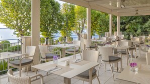 A covered outdoor dining area with tables and chairs, overlooking a body of water and greenery.