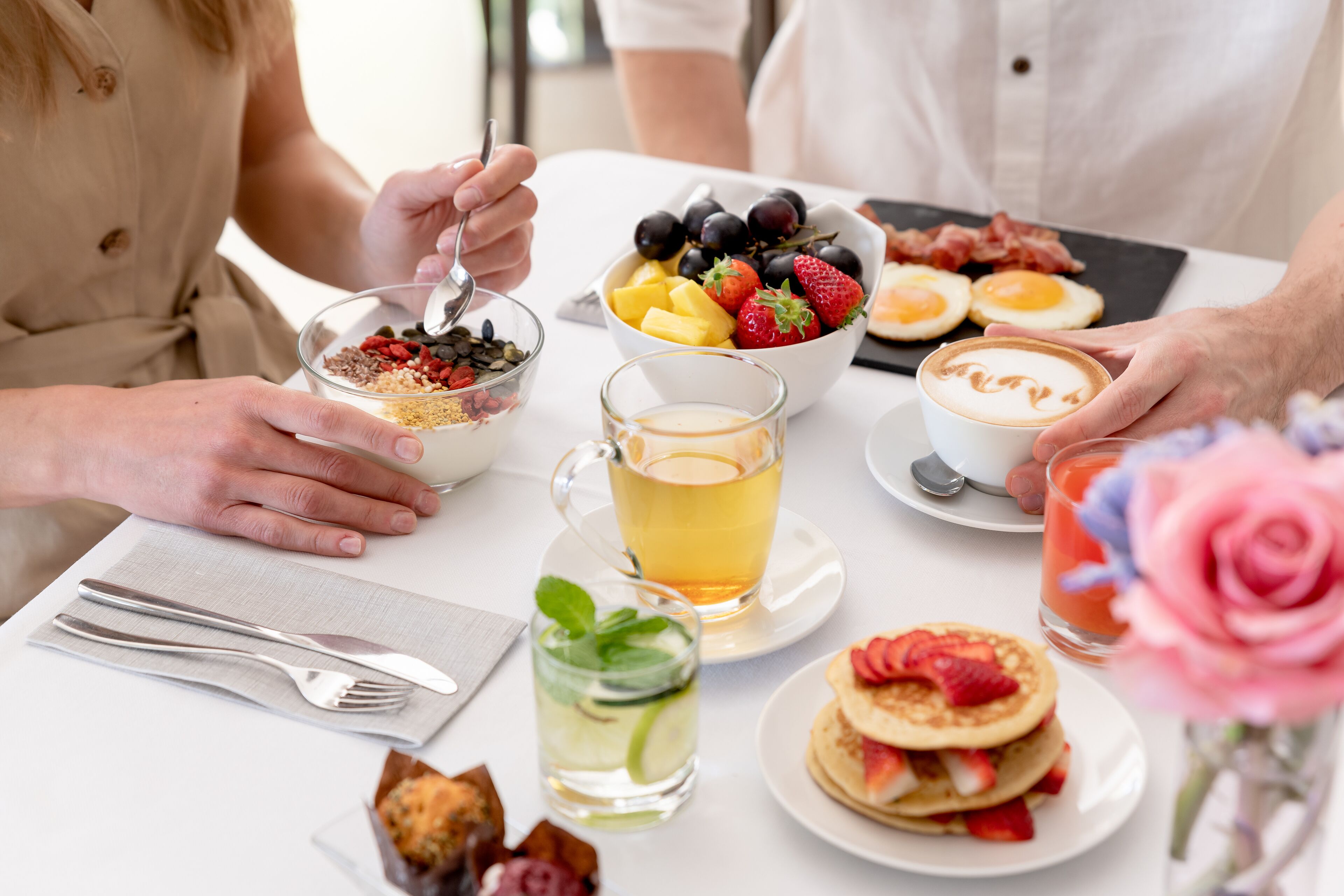 Una escena de desayuno con diferentes alimentos, una taza de té y un vaso de jugo sobre una mesa.