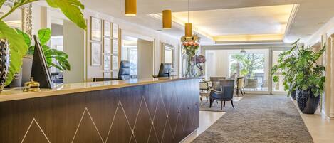 A reception area with a dark wooden reception desk, framed certificates on the wall, and a carpeted floor.