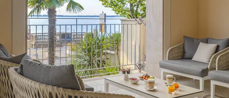 A balcony with wicker furniture, a table with breakfast items, and a view of the sea.