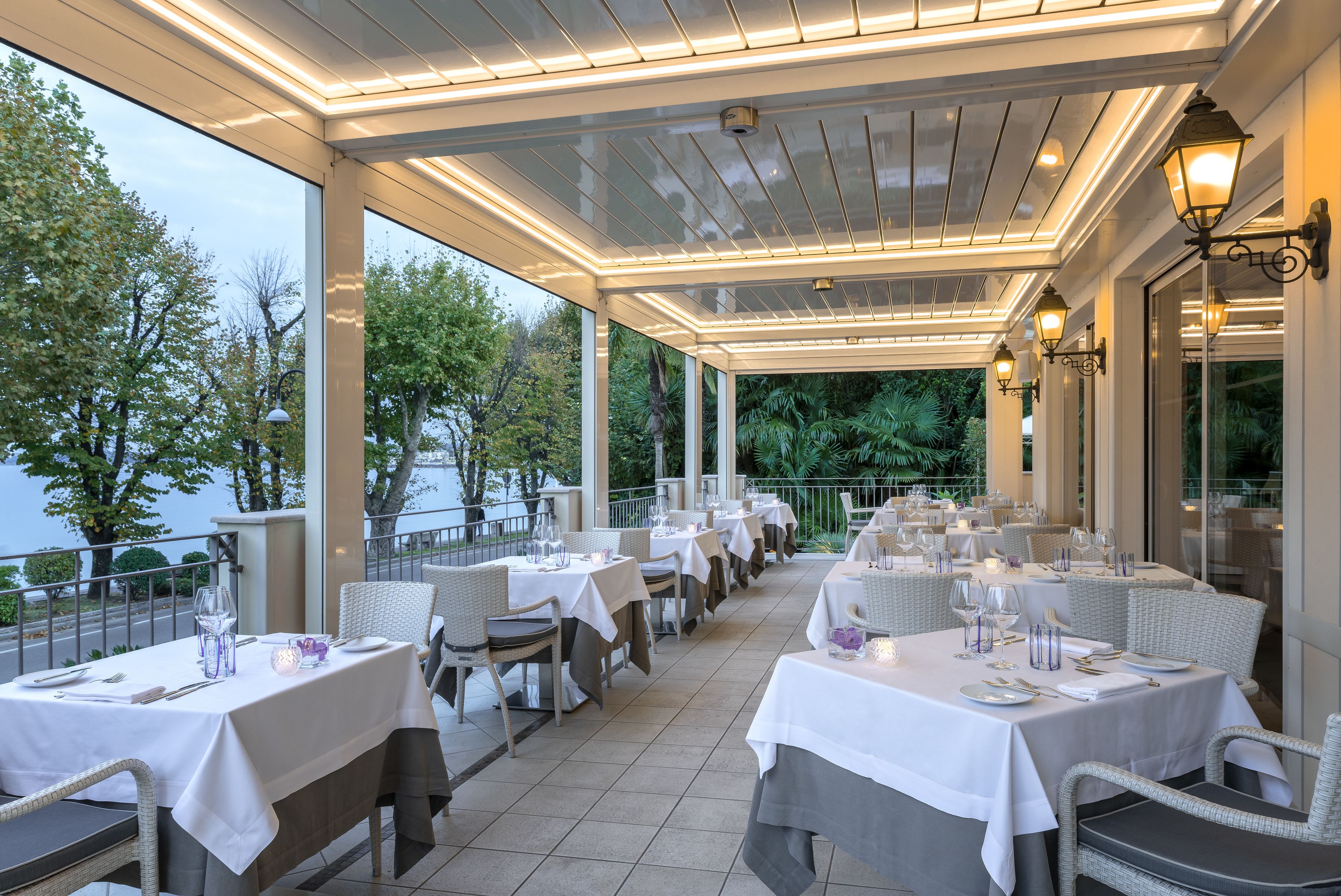 An outdoor dining area with tables set for two, overlooking a body of water.