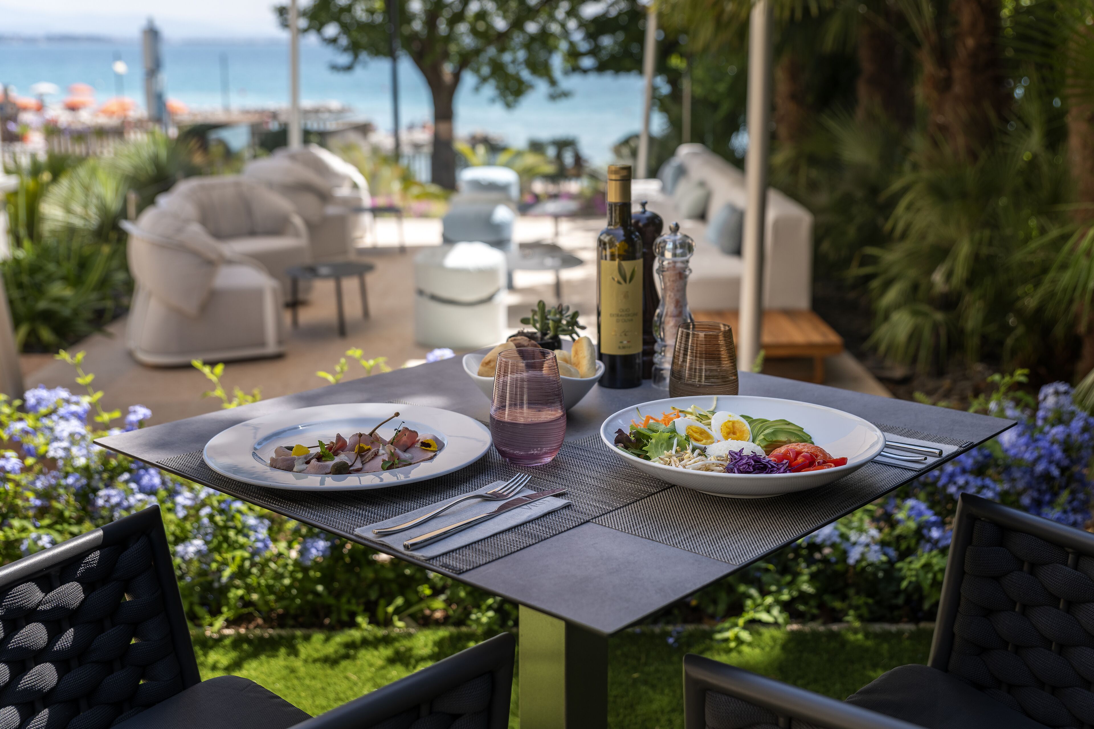 An outdoor dining area with a table set for two, featuring plates of food, a pitcher, and bottles of wine.