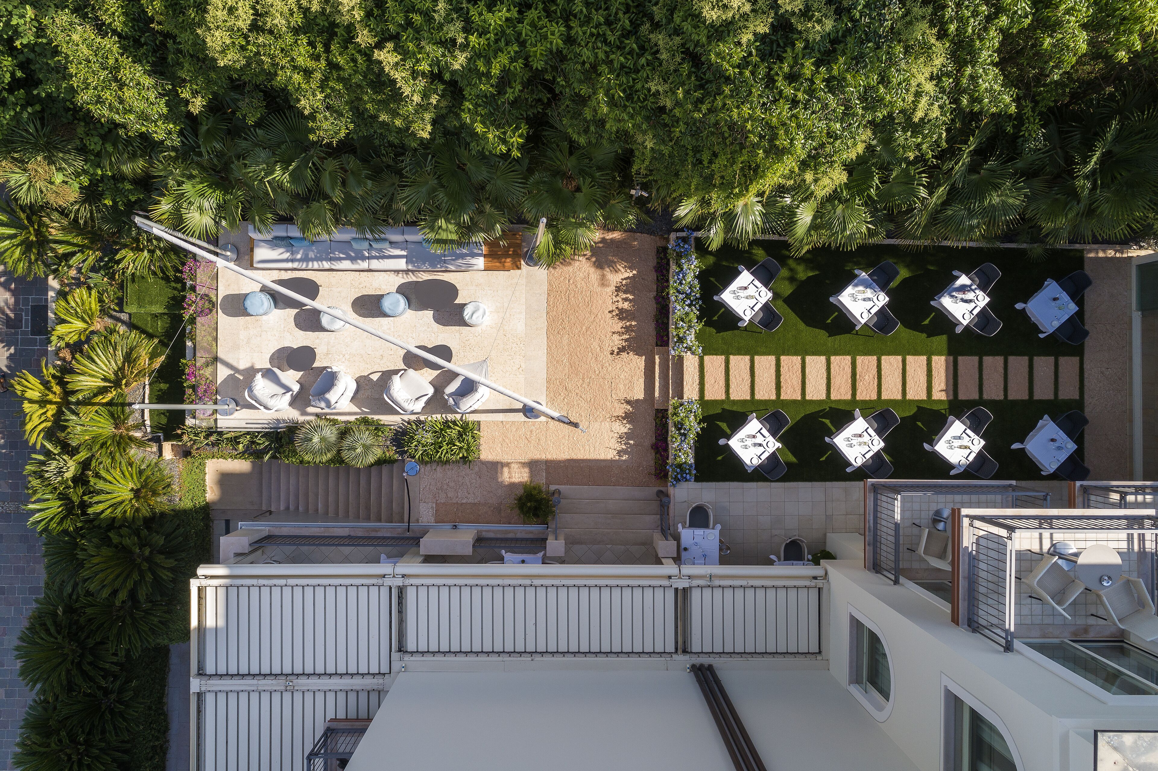 Vista aérea de una terraza en la azotea con varias zonas de estar, una piscina y abundante vegetación.
