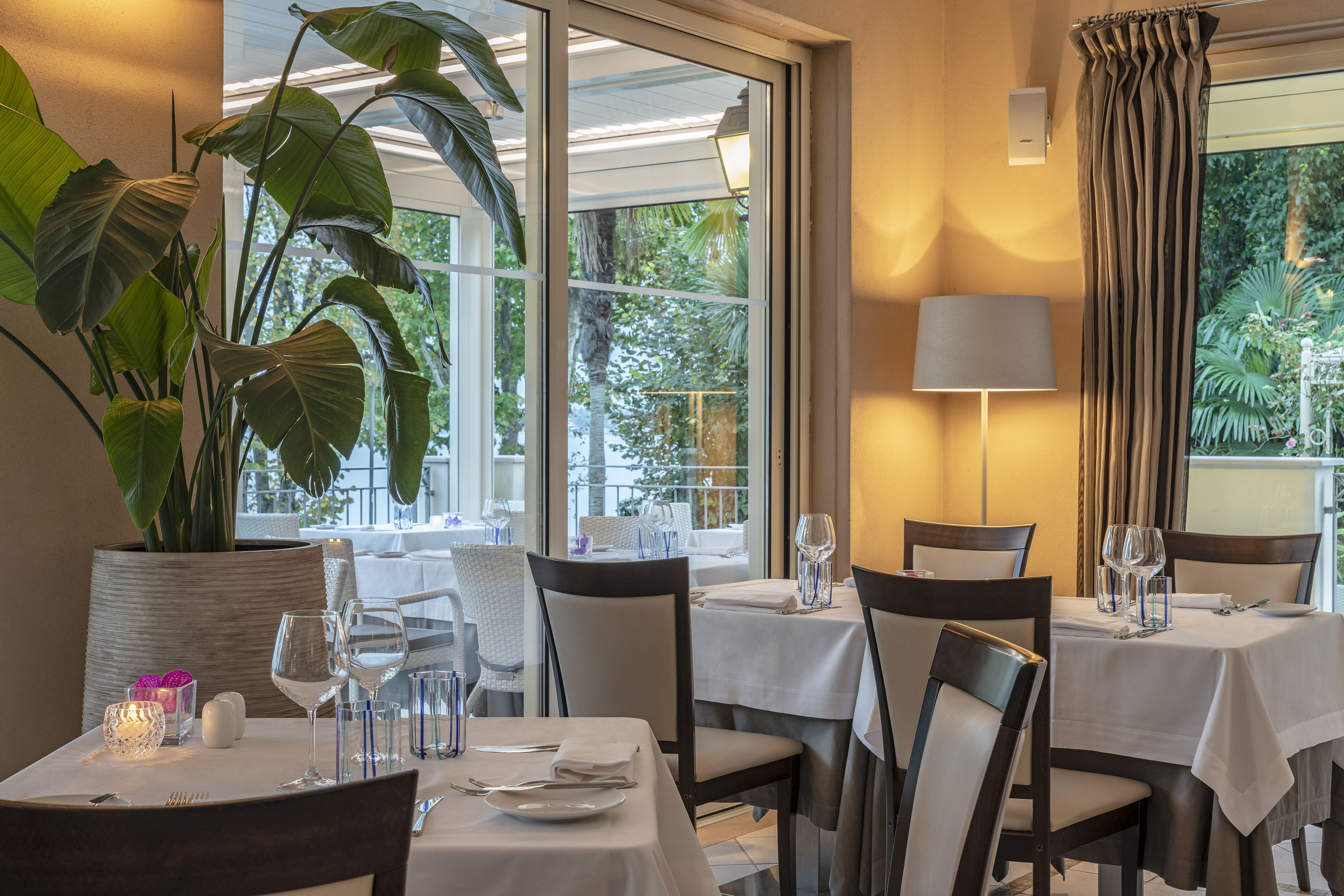 En restaurang med bord dukade för middag, stora krukväxter och utsikt över omgivningarna.