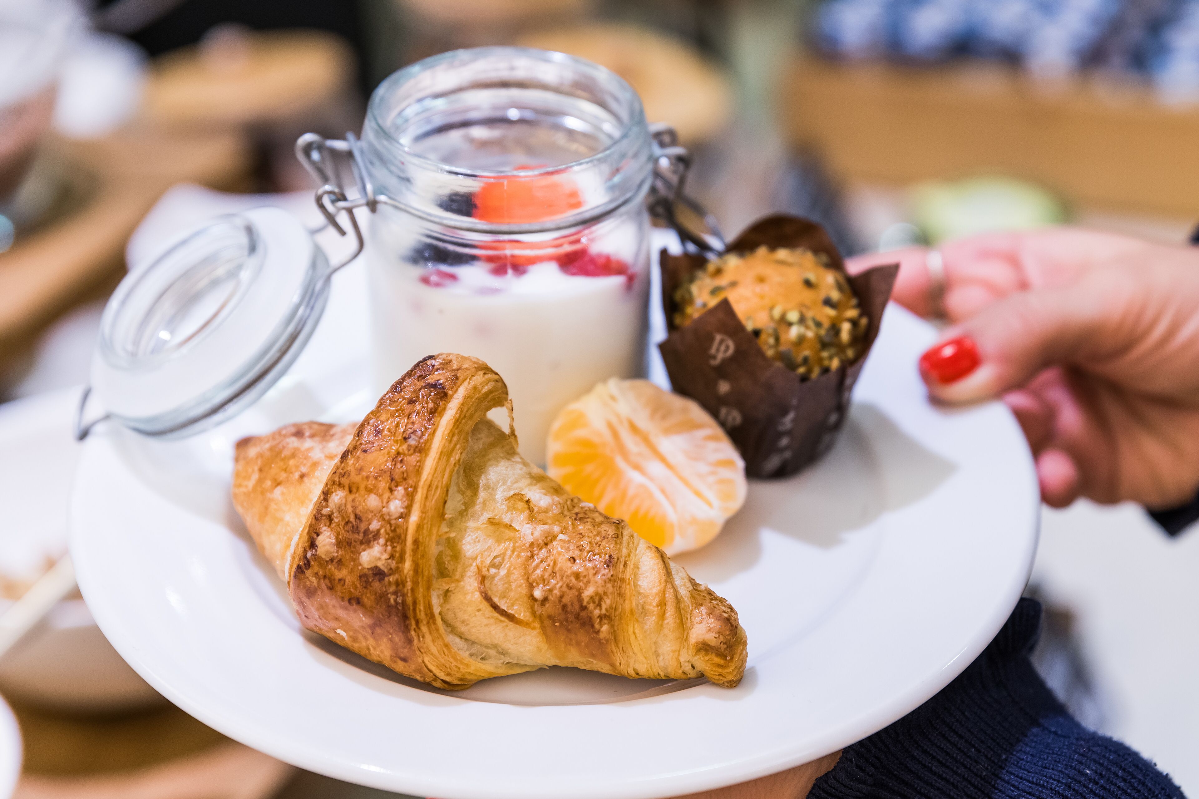 A plate with croissants, a glass jar of yogurt with fruit, and a chocolate-covered pastry.