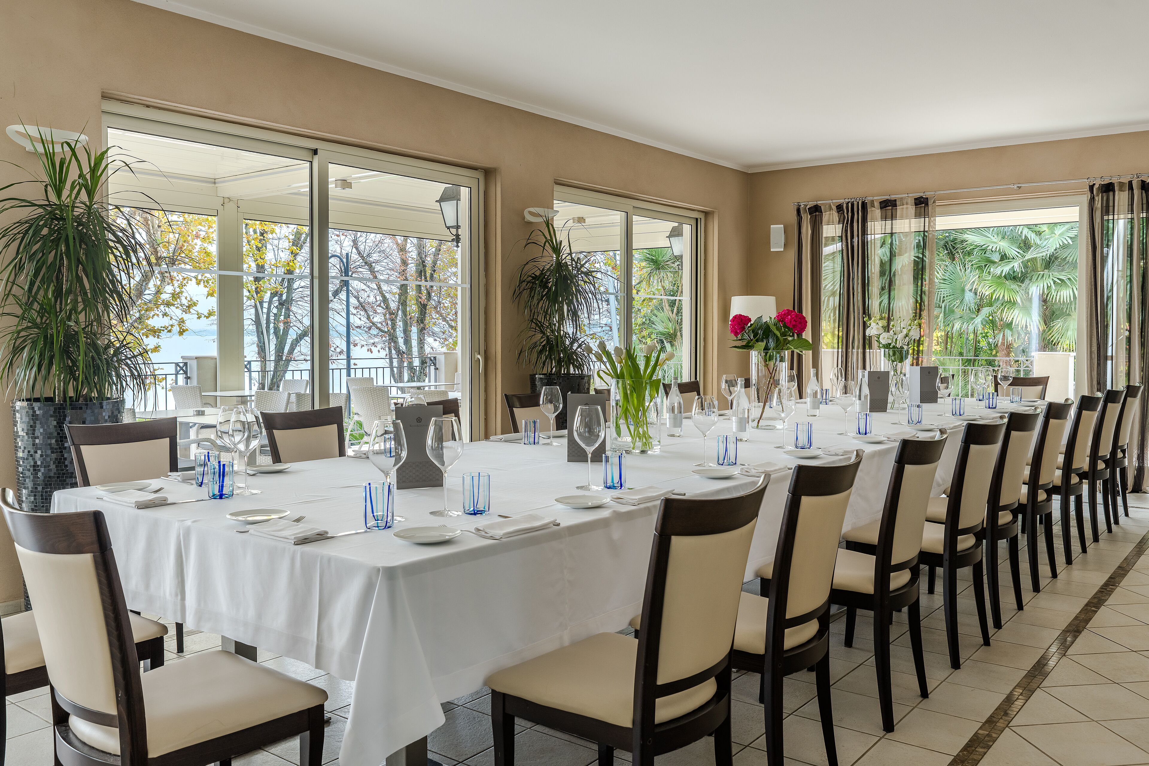 A long dining table set for a formal meal with chairs, glassware, and a vase with flowers.