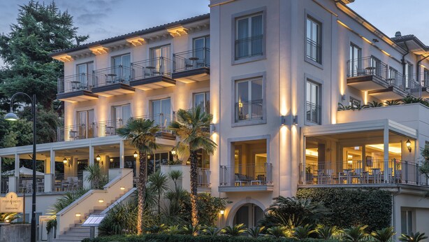 A multi-story hotel with balconies, outdoor seating, and a well-lit entrance. - Villa Rosa Hotel (Desenzano del Garda)