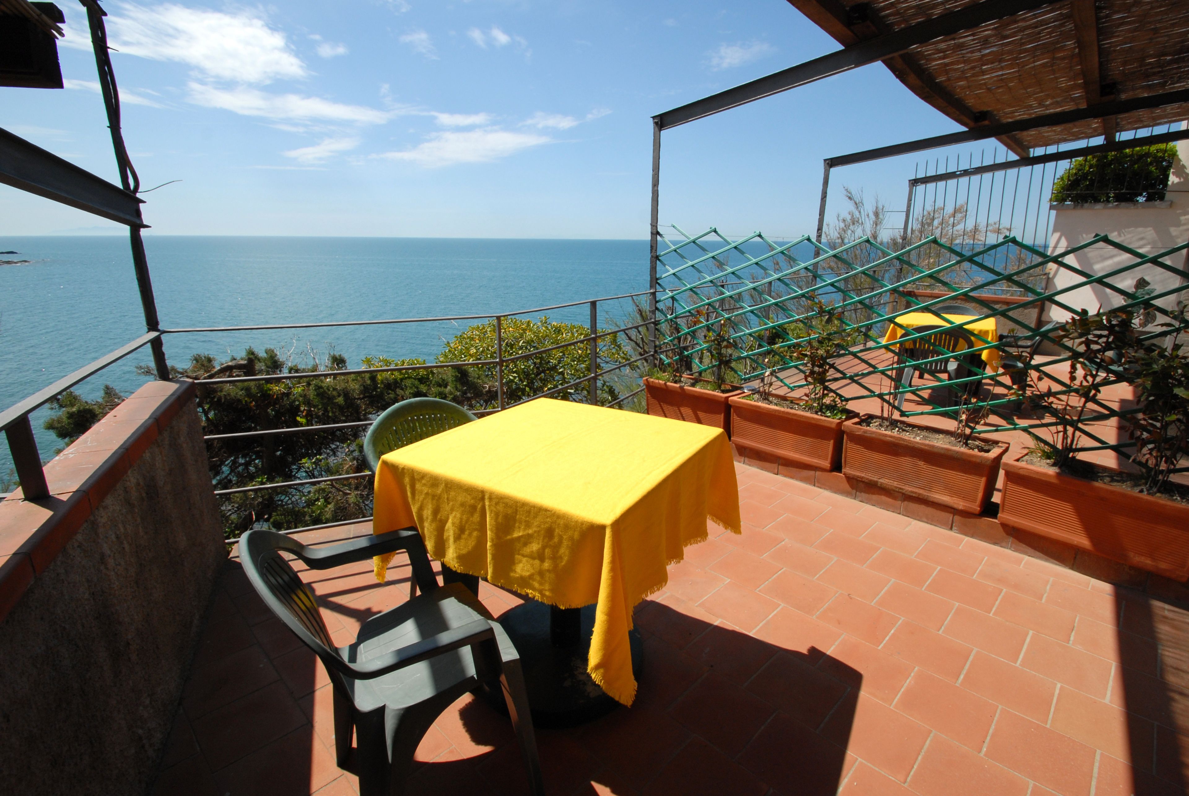 A terrace with a yellow table and chairs, overlooking a coastal view.
