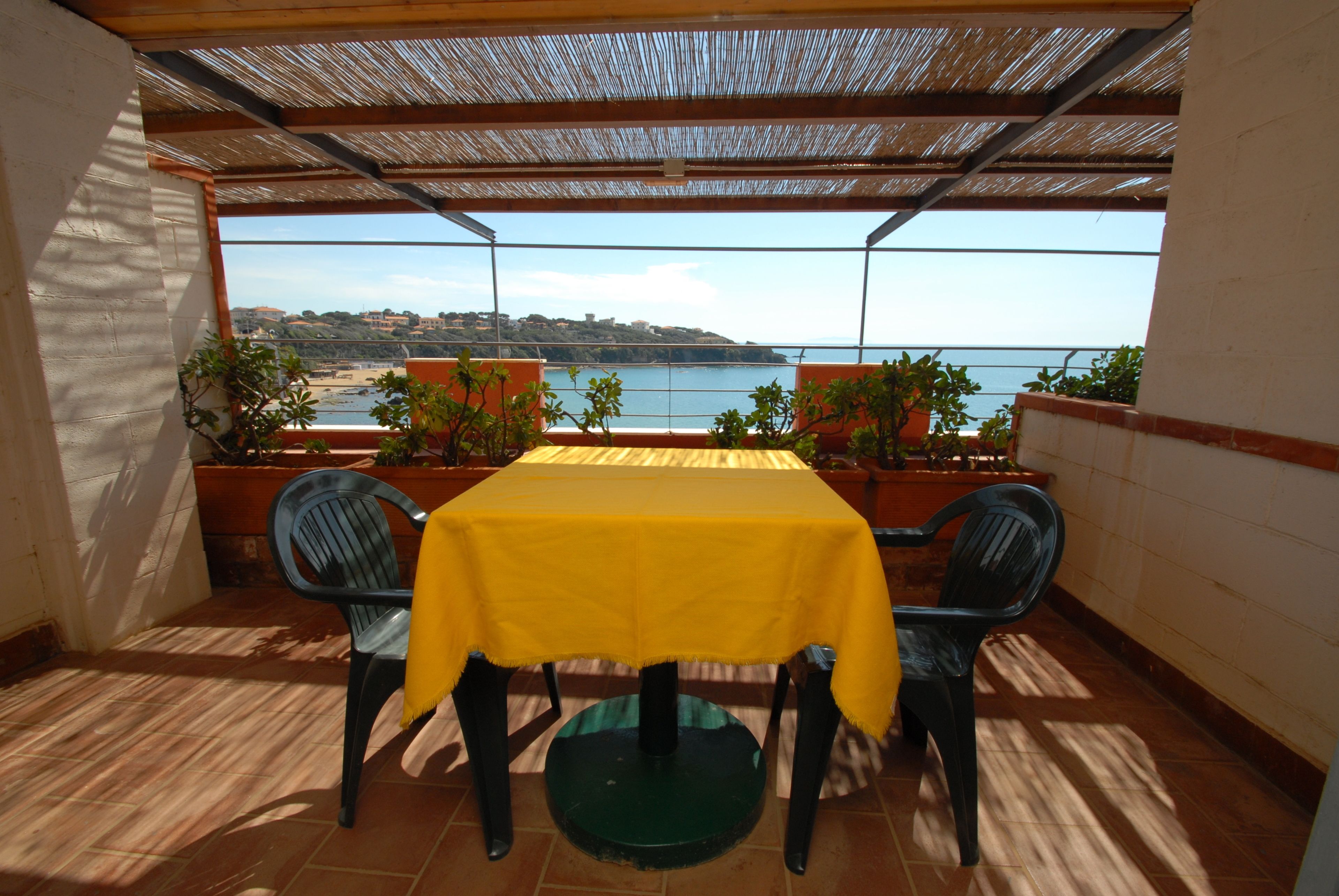 Une terrasse couverte avec une table et des chaises, donnant sur une plage et la mer.