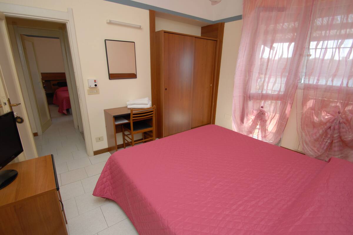 A bedroom with a bed, a desk, a chair, a wardrobe, and a television.