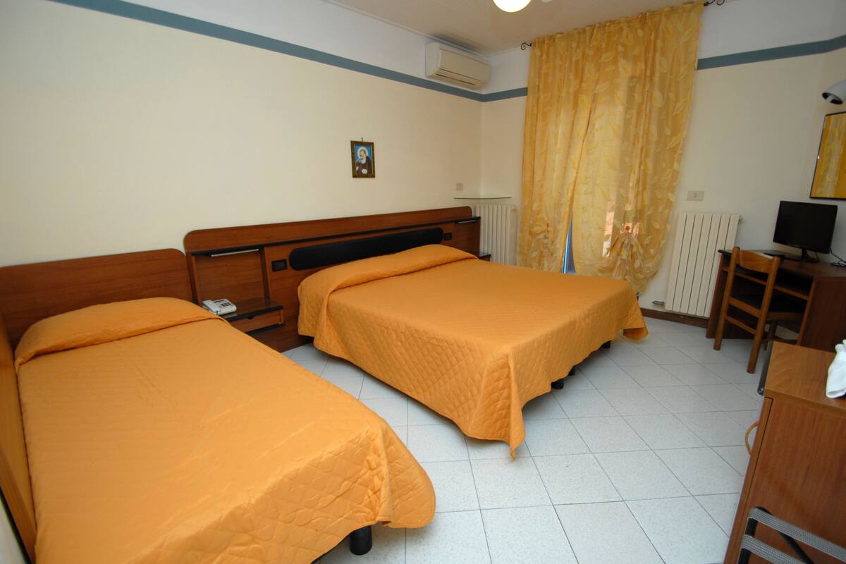 A hotel room with two single beds, a desk with a computer, a chair, and a radiator.