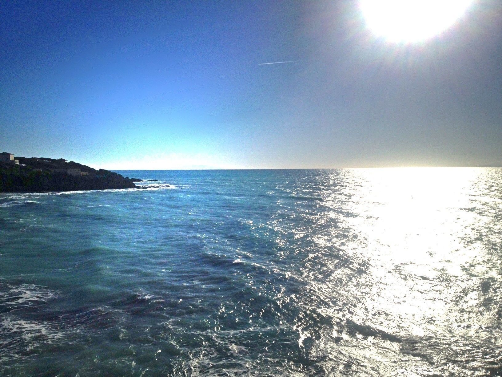 A coastal scene with a clear sky and sunlight reflecting off the water.