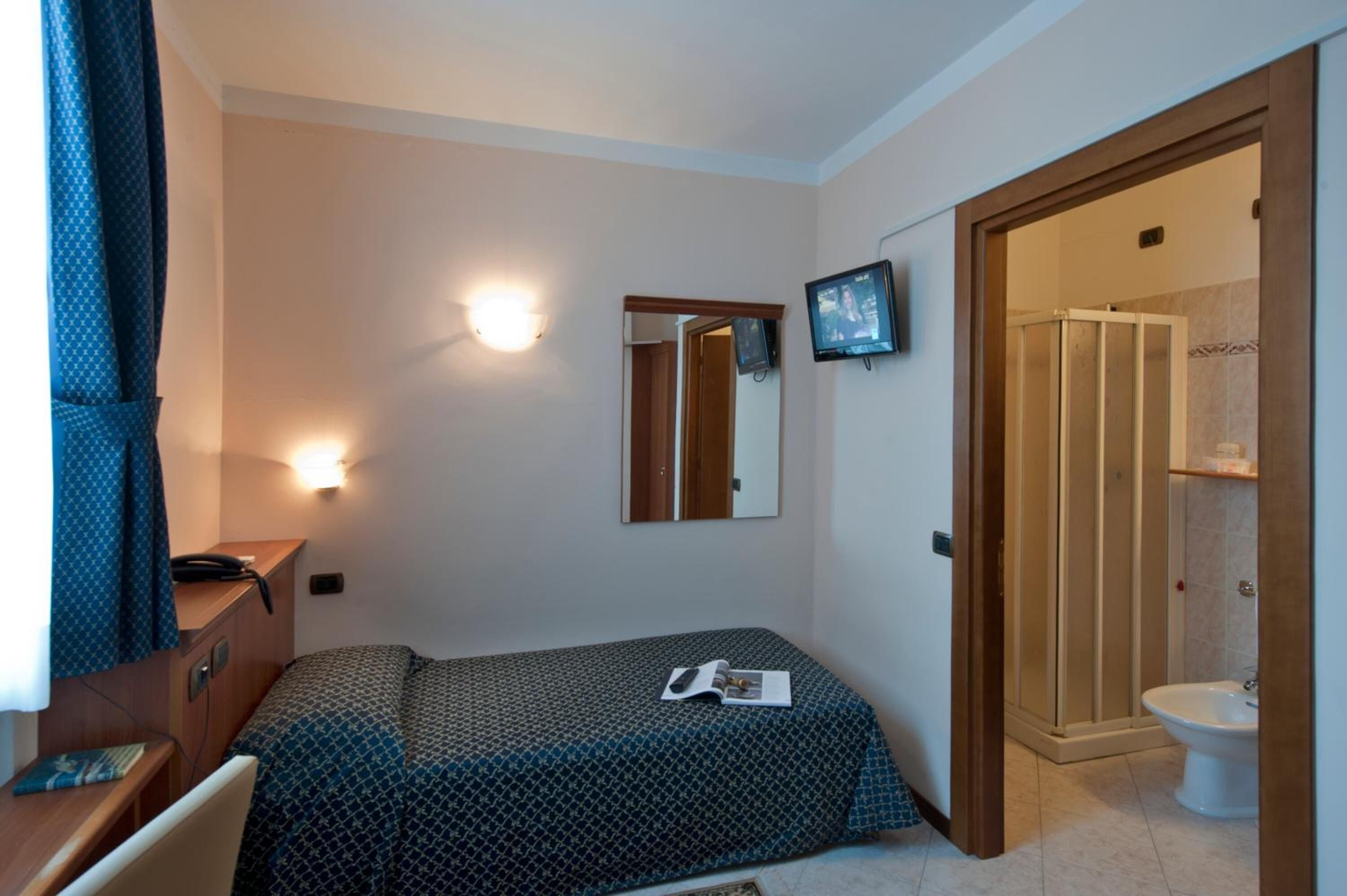 A small, neatly arranged bedroom with a bed, bedside table, mirror, and a TV mounted on the wall.